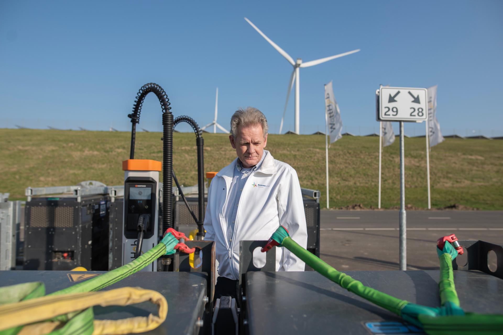 Tom Rensen staat bij het snellaadplein in Geldermalsen. Je ziet groene kabel en op de achtergrond windmolens.